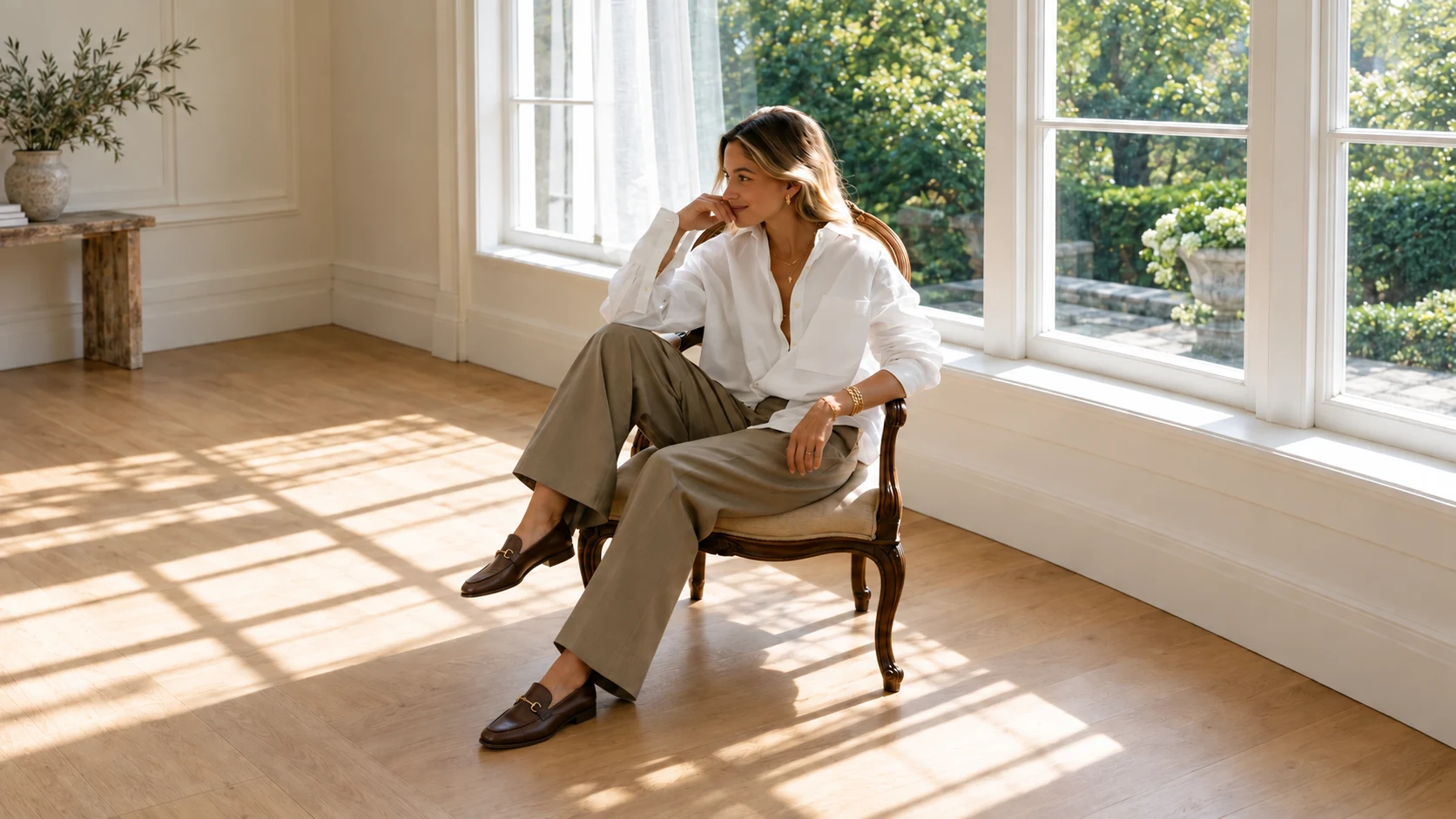 Camille in leather loafers seated by the garden windows, with her full chair and the warm wooden studio floor in view.